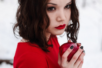 Snow white in red dress in winter forest with apple in hands