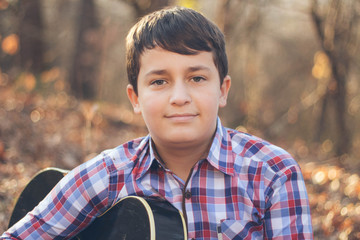 Teenage boy playing guitar in a sunny autumn day