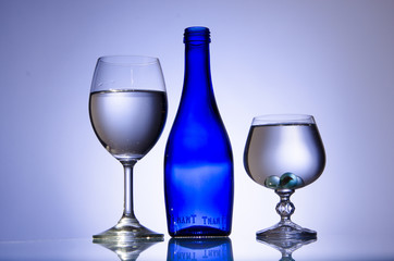 Blue bottle and two stemware of water on white background
