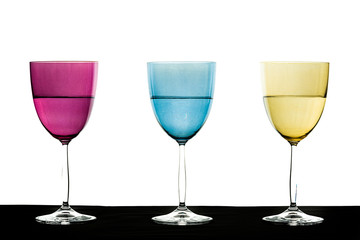 verres à pied colorés un rose un bleu un jaune à moitié plein sur un fond blanc