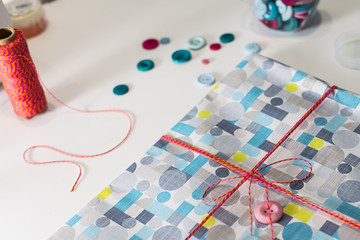 Gift present con colorful wrap paper and decoration buttons on a white table