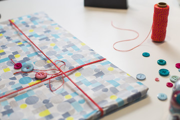 Gift present con colorful wrap paper and decoration buttons on a white table
