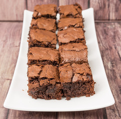 Homemade chocolate brownies in white plate over wooden background