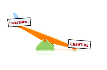 image concept of unbalance word INVESTMENT on top and CREATIVE at bottom.green and orange color toy seesaw isolated white background