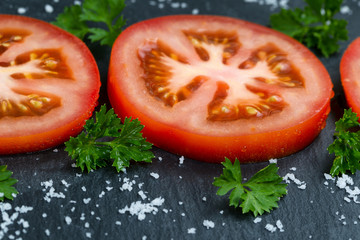 Freshly sliced ripe tomato on black slate stone background