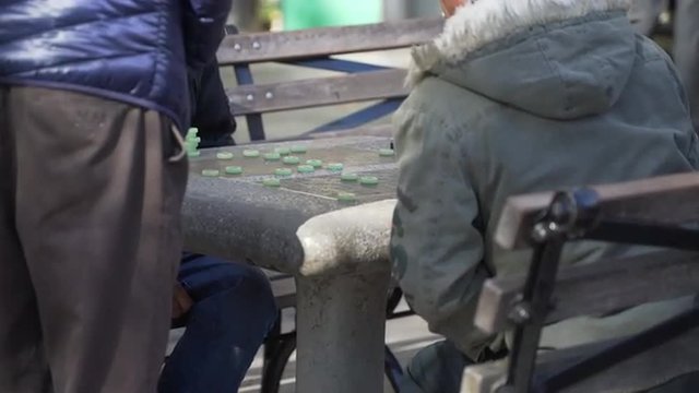Three Asian men play checkers (Chinese?) in a park in the cool Fall weather