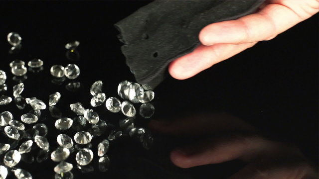 SUPER SLOW (240fps): A human hand fall out a lot of a diamonds from a pouch on a black table
