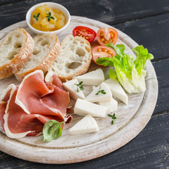 ham, cheese, tomatoes and ciabatta bread served on a light wooden board on a dark wooden surface. Tasty Breakfast, snack or delicious appetizer to wine