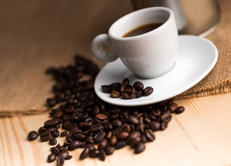 Brown coffee grains and a hot white cup on a wooden backgroud