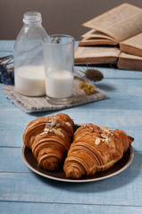 Two croissants with almonds and milk on blue wooden surface