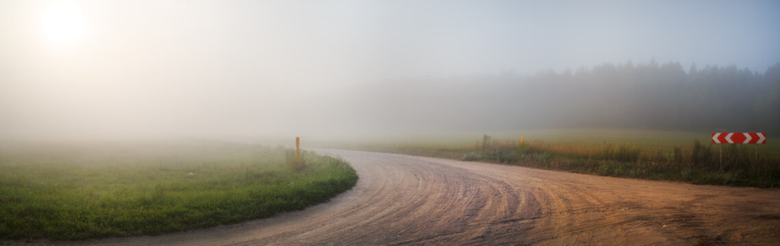 Gravel road in the fog. Turn of gravel road. Rural landscape. Panoramic shot. Toned image.