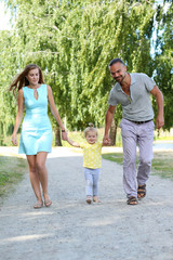 Happy parents with daughter outdoor holding her hands