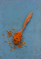 Dried yellow petals Jerusalem artichoke in a wooden spoon on old blue table. Ingredient for cooking healthful beverage. The concept of rustic herbal therapy