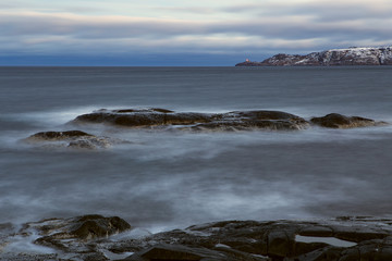 Stone beach and the lighthouse on the cape. Barencevo sea. Kola Peninsula. Murmansk region. Russia.