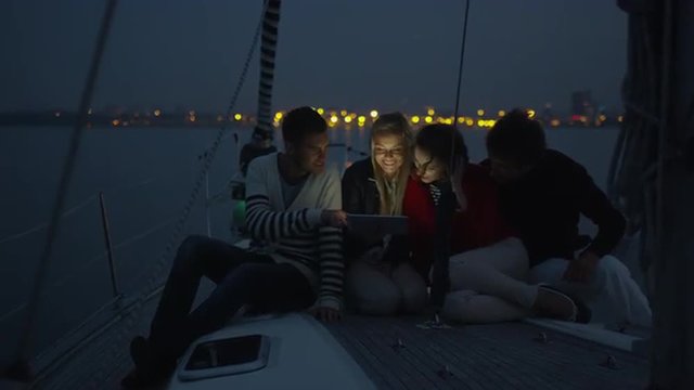 Group of people are using tablet on a yacht in the sea at night. Shot on RED Cinema Camera.