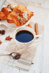 sweet breakfast or lunch, a cup of black coffee and croissants with almonds , nuts and cinnamon on a wooden background