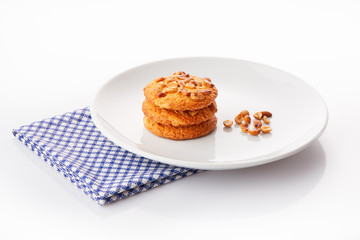Stack of three homemade peanut butter cookies and peanuts on white ceramic plate on blue napkin, isolated on white background