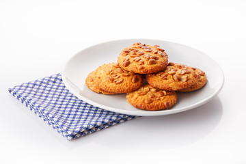 Pile of homemade peanut butter cookies on white ceramic plate on blue napkin, isolated on white background