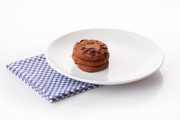 Stack of three homemade chocolate chip cookies on white ceramic plate on blue napkin, isolated on white background