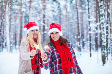 two girls in Christmas hats with sparklers in the winter forest