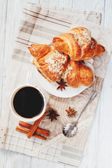 sweet breakfast or lunch, a cup of black coffee and croissants with almonds , nuts and cinnamon on a wooden background