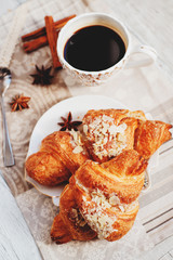 sweet breakfast or lunch, a cup of black coffee and croissants with almonds , nuts and cinnamon on a wooden background