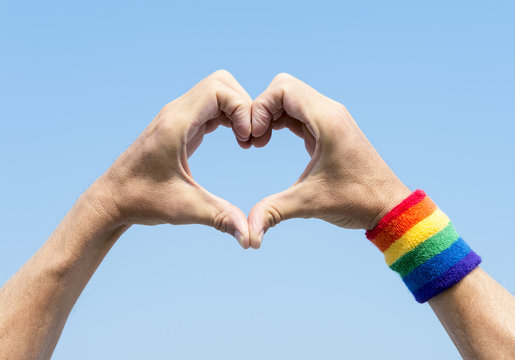 Gay athlete making hand heart with gay pride rainbow colors wristband against bright blue sky