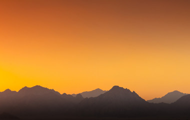 Orange and yellow sunset above layers of mountains.