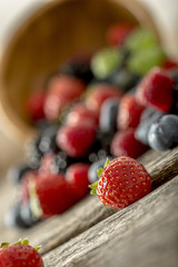 Closeup of juicy ripe mixed berry fruits scattering out of woode