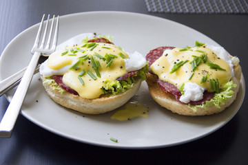 Eggs Benedict dish consisting of poached eggs and sliced ham on toasted English muffins, covered with hollandaise sauce against a dark background.