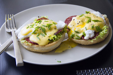 Eggs Benedict dish consisting of poached eggs and sliced ham on toasted English muffins, covered with hollandaise sauce against a dark background.