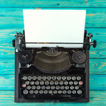 Typewriter with inserted blank clean white paper on a blue wooden table. Top view. Cool artist author writer background. Toned tinted filtered square photo instagram retro vintage style