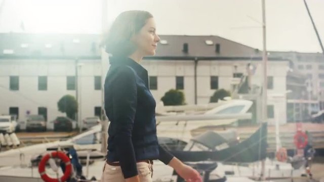 Beautiful woman walking around sea port with yachts on a sunny day. Shot on RED Cinema Camera.