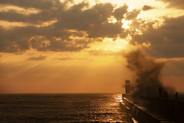 Group of fishermen on the pier near lighthouse with wave splash