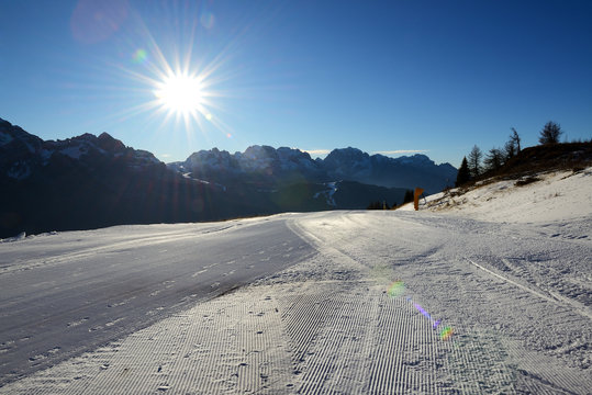 The ski slope with a view on Dolomiti mountains and sun, Madonna