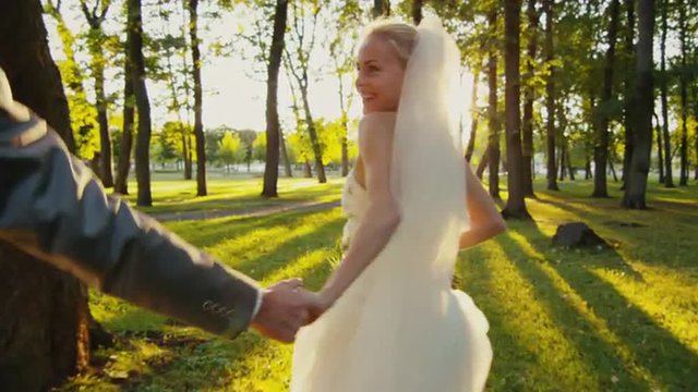 Smiling bride holds groom by the hand and runs in a park