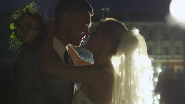 Happy young newlyweds are kissing next to fireworks in a park in the evening. Shot on RED Cinema Camera.