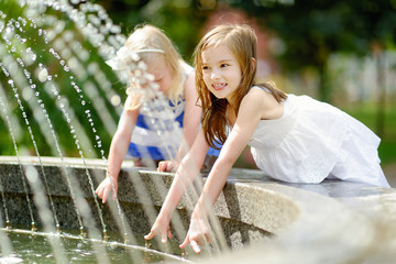 Two cute little girls playing with a city fountain