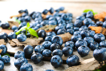 Tasty ripe blueberries with green leaves on wooden table close up