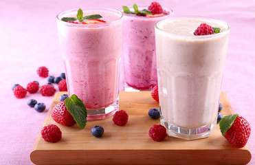 Milkshakes at cutting board with berries on light background
