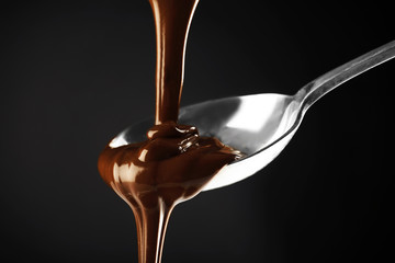 Chocolate poured on a spoon on dark background