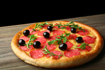 Tasty pizza with salami and olives on wooden table against black background
