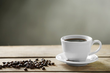 Cup of coffee and coffee grains on wooden table, on gray background