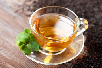 Glass cup of tea with green leaves on wooden background decorated with scattered tea