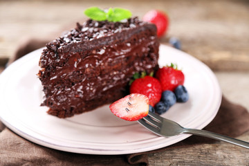 Chocolate cake with chocolate cream and fresh berries on plate, on wooden background