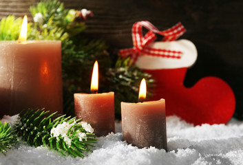 Burning candles and Christmas accessories with snow on wooden background