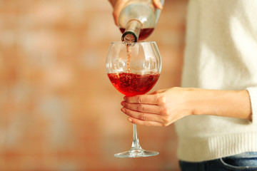 Young woman pouring pink wine into glass on blurred background