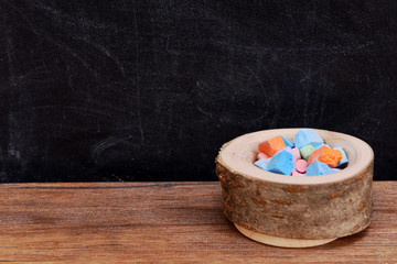 Obraz na płótnie Canvas Wooden bowl of coloured chalk on desk in front of blackboard