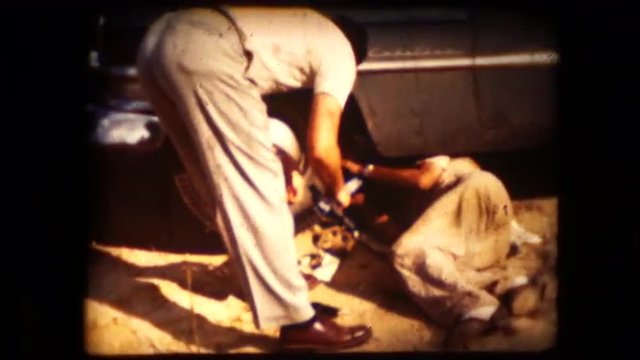 Two men work to repair a broken down car in the mid 1960's