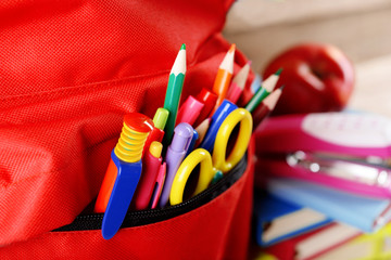 Obraz premium Full of stationary red backpack and pile of books with apple on top on wooden background, close up